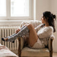 Woman wearing dog print knee high socks sitting on a chair in a cozy room with light-colored walls and wooden floor.