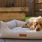 Dog lying on a textured pet bed outdoors with wooden furniture in the background