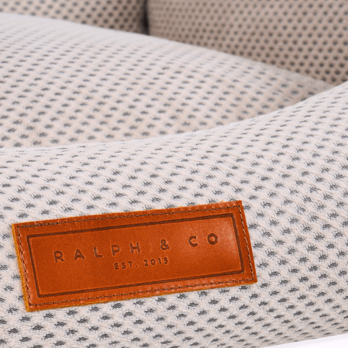 Textured fabric surface with a brown leather label displaying 'Ralph & Co' on a blurred background.