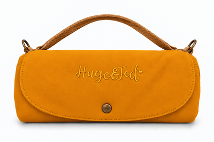 A mustard yellow faux suede clutch bag with a brown woven top handle, featuring the embroidered brand name 'Hugo & Ted' on the front flap and a gold snap button closure.
