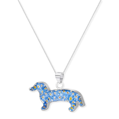 A silver dachshund-shaped pendant necklace filled with small blue flowers and yellow centers, hanging from a delicate silver chain against a plain white background.