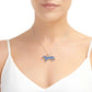 A close-up of a model wearing a silver necklace with a dachshund-shaped pendant decorated with blue and gold accents, paired with a white camisole top against a white background.