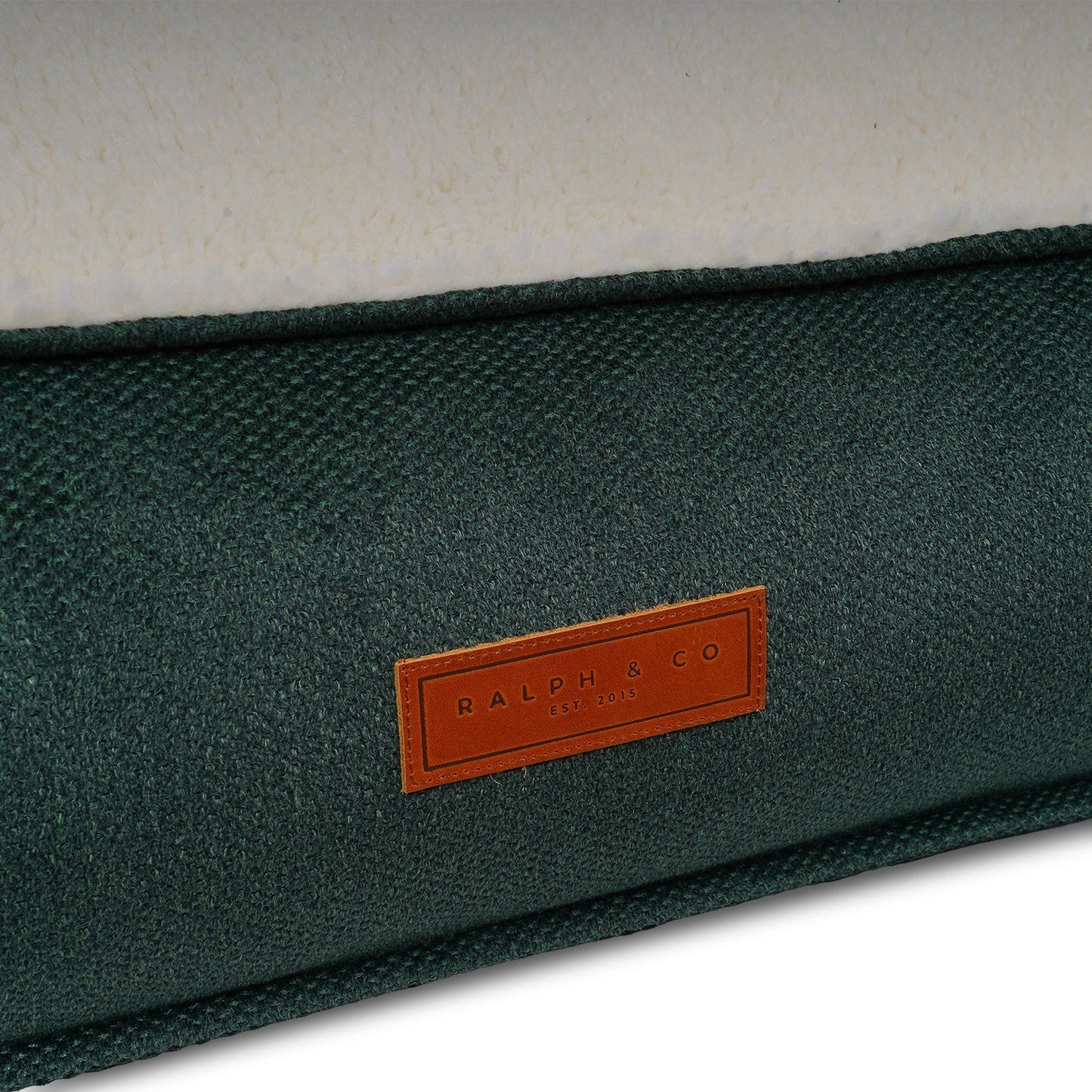 Close up of Green fabric dog bed surface with a brown leather label featuring 'Ralph & Co' branding.