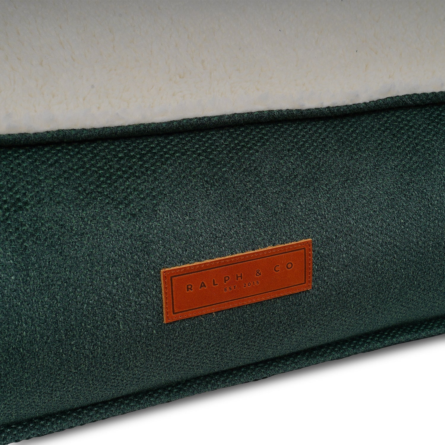 Close up of Green fabric dog bed surface with a brown leather label featuring 'Ralph & Co' branding.
