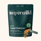 A dark teal stand-up pouch of superwild Super Everyday dog supplement, shown on a light beige background with a scoop of the brown powder in front.