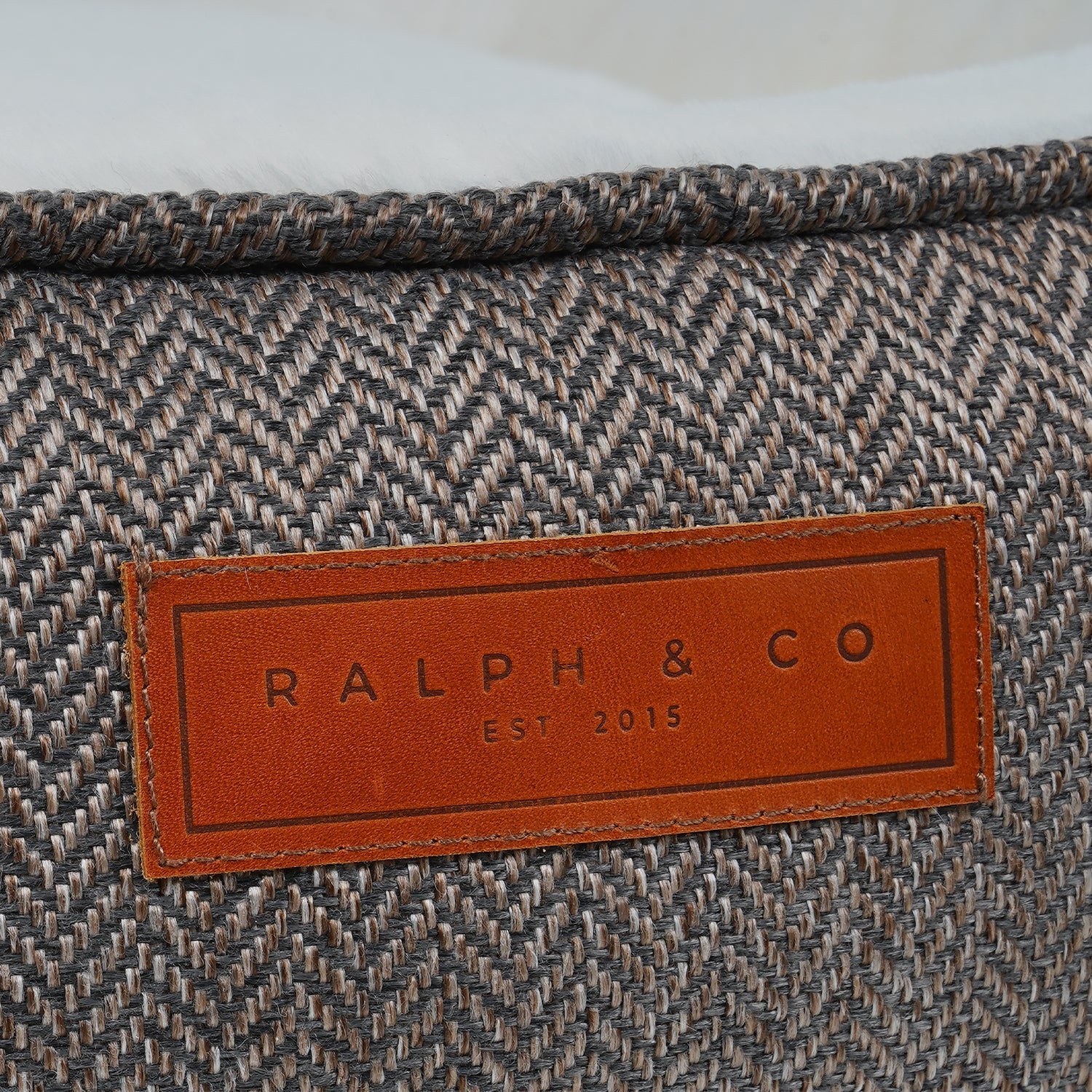 Close-up of a textured fabric surface with a brown leather label displaying 'RALPH & CO' branding.