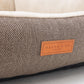 Brown textured pet bed with a leather label on a light gray background