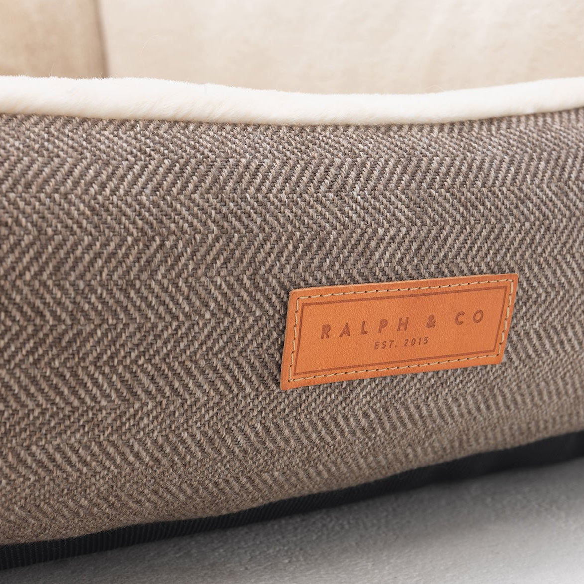 Brown textured pet bed with a leather label on a light gray background